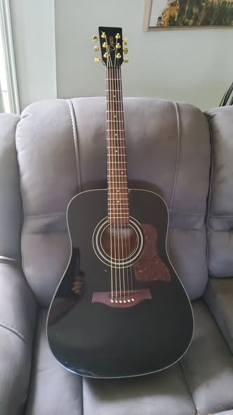 Black Travis acoustic fully restored and restrung after top crack repair, resting on a sofa